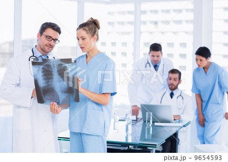 Doctors examining x-ray with colleagues using laptop behind 9654593