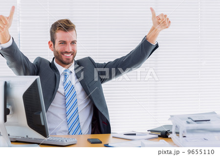 Cheerful businessman gesturing thumbs up at office desk Cheerful businessman gesturing thumbs up at office desk 9655110