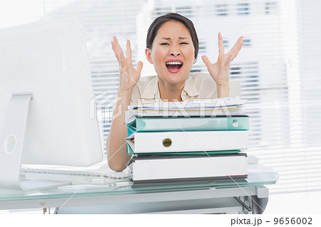 Angry businesswoman shouting with stack of folders at desk Angry businesswoman shouting with stack of folders at desk 9656002
