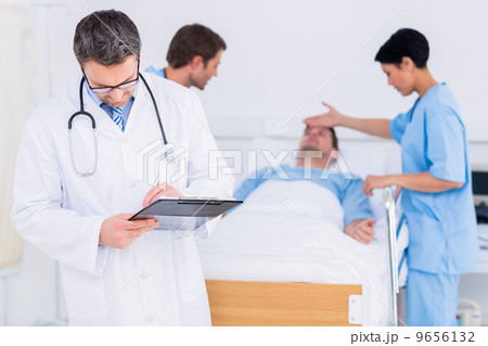 Doctor writing reports with patient and surgeon in background 9656132