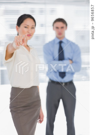 Businesswoman pointing towards camera with man in office Businesswoman pointing towards camera with man in office 9656857