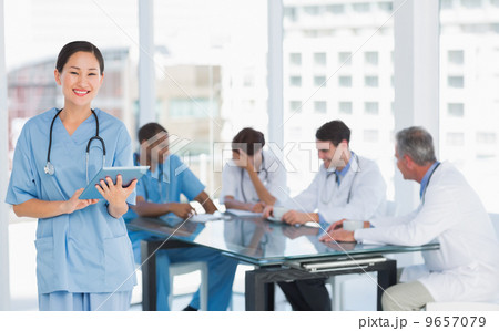 Surgeon using digital tablet with group around table in hospital 9657079
