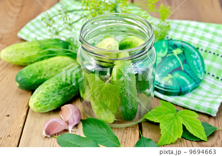 Cucumbers in jar with leaves and napkin on the board 9694663