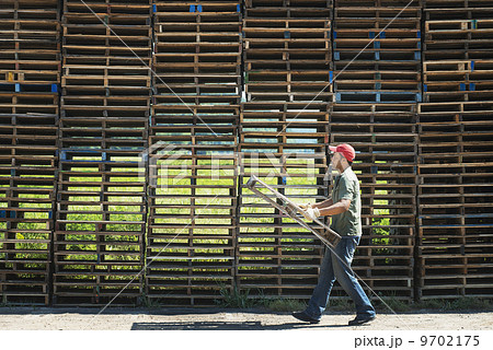 A man carrying a wooden plant frame or pallet in front of a huge stack of objects. A man carrying a wooden plant frame or pallet in front of a huge stack of objects. 9702175
