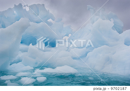 Melting icebergs with ice formations and shapes with holes, floating on the waters off the shores of East Greenland 9702187