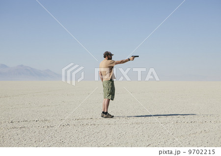 Man aiming hand gun, standing in vast, barren desert 9702215