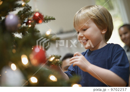 A young boy holding Christmas ornaments and placing them on the Christmas tree. 9702257