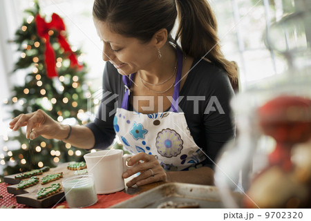 A woman working on organic homemade Christmas cookies, decorating and sprinkling decorations on green icing. 9702320