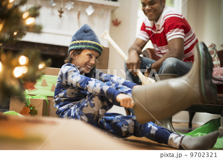 A boy by a Christmas tree unwrapping a gift, and trying on muck boots. A boy by a Christmas tree unwrapping a gift, and trying on muck boots. 9702321