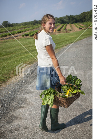A girl in boots on a farm carrying a basket full of fresh produce. A girl in boots on a farm carrying a basket full of fresh produce. 9702412