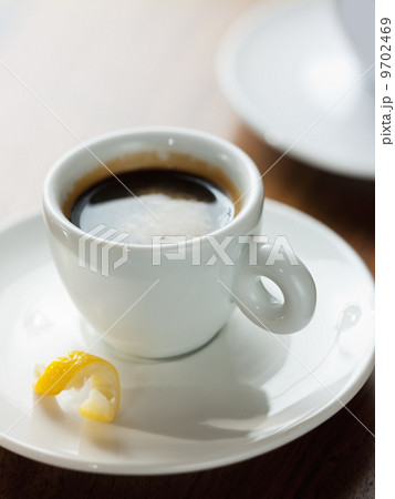 A cup of black coffee in a white china cup with a small twist of lemon peel in the saucer. 9702469