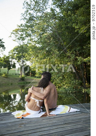 A young couple, boy and girl, sitting close together on a wooden jetty by a water pool. A young couple, boy and girl, sitting close together on a wooden jetty by a water pool. 9702519