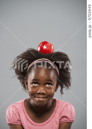A girl concentrating on sitting still with a large red apple balanced on her head. A girl concentrating on sitting still with a large red apple balanced on her head. 9702649