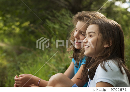 Two children, girls sitting side by side, laughing in the fresh air. 9702671