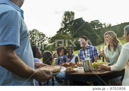 A family and friends sitting at a tabe outdoors having a meal. A family and friends sitting at a tabe outdoors having a meal. 9702806