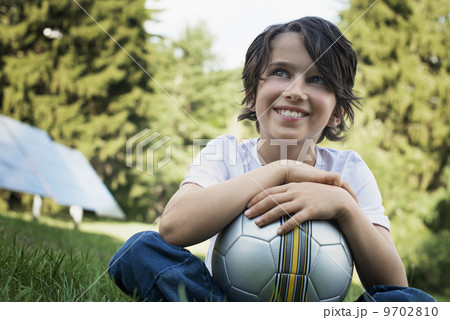 A boy holding a football, sitting on the grass. Solar panels. 9702810