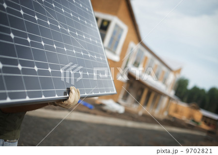 A workman carrying a large solar panel at a green house construction site. 9702821