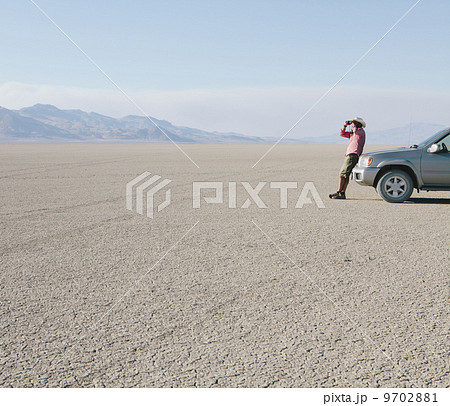 A man leaning against a truck, looking through binoculars. A man leaning against a truck, looking through binoculars. 9702881