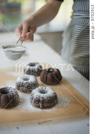 A woman dusting fresh made chocolate buns with icing sugar. A woman dusting fresh made chocolate buns with icing sugar. 9702913