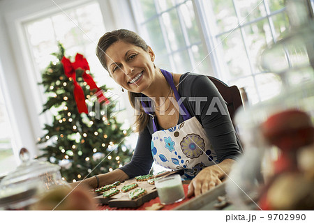A woman working on organic homemade Christmas cookies, decorating and sprinkling decorations on green icing. 9702990