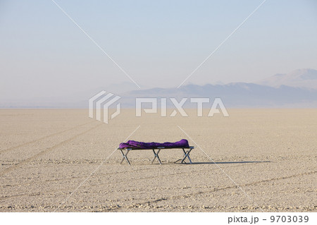 Sleeping bag on cot in vast, barren desert, dawn 9703039