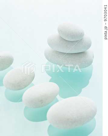 Smooth white pebbles of uniform size and colour displayed on a blue reflective glass background. Smooth white pebbles of uniform size and colour displayed on a blue reflective glass background. 9703041