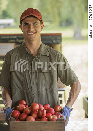 Organic farmer, young man holding baskets of fresh fruit at a market farm stand. 9703058