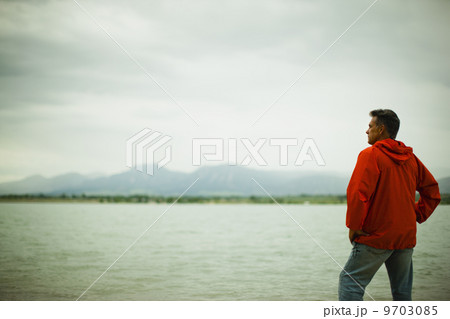 A middle aged man in a red jacket looking over water, deep in thought. A middle aged man in a red jacket looking over water, deep in thought. 9703085