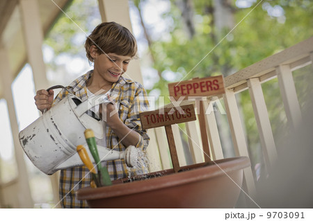 A child holding a watering can, watering a a pot with newly planted tomato and pepper seeds. 9703091