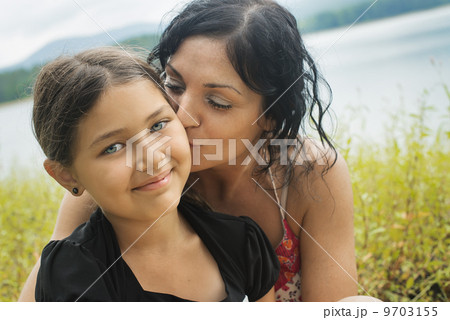A mother and daughter in long grass by a lake shore. 9703155