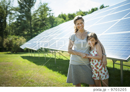 A child and her mother in the fresh open air, beside solar panels on a sunny day at a farm in New York State, USA. 9703205