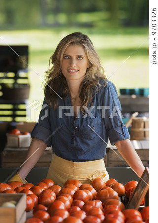 Organic farmer, a woman standing at a farm stand stall. Display of tomatoes. 9703326