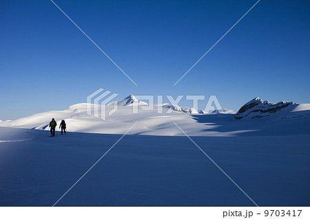 Two skiers on a slope taking in the view of the mountainous landscape of the Wapta Traverse in the Rocky Mountains. 9703417