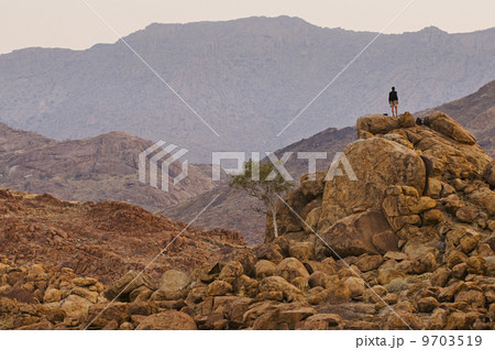 A person standing on a rock pile overlooking Brandberg, Tsiseb Conservancy, Damaraland, Namibia 9703519