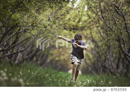 A child running along a natural woodland tunnel with tree branches forming an arch. 9703595