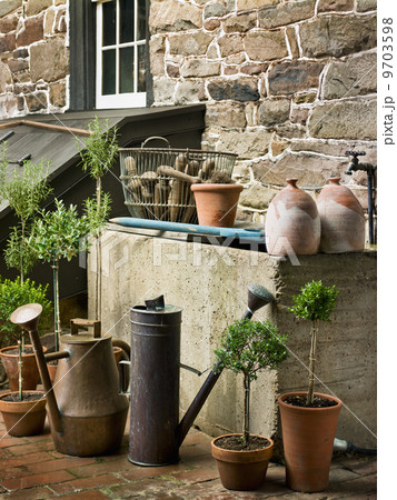 A collection of old watering cans, and clay pots for plants, outside a house. A collection of old watering cans, and clay pots for plants, outside a house. 9703598
