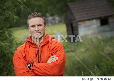 A young man with his arms folded in a bright orange jacket. 9703638
