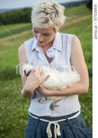 A young girl, teenager, holding a chicken with white feathers in her arms. 9703669