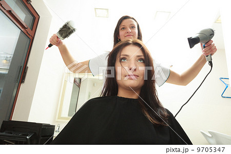 In hairdressing salon. Hairstylist with dryer drying hair of woman client. 9705347