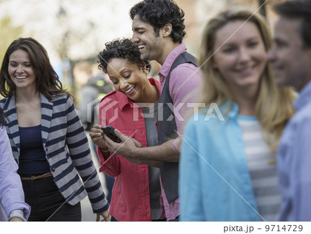 People outdoors in the city in spring time. A group of men and women, two looking at a cell phone screen and laughing. People outdoors in the city in spring time. A group of men and women, two looking at a cell phone screen and laughing. 9714729