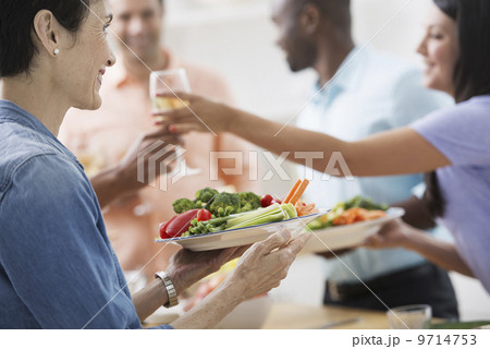 An open plan office in New York City. A working lunch, a salad buffet. A group of men and women of mixed ages and ethnicities meeting together.  A woman holding out a glass of wine, and a plate of food.  9714753