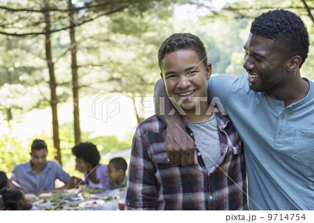A family picnic meal in the shade of tall trees. A man and a young boy looking at the camera. 9714754