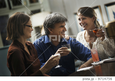 Three people meeting for a drink. Two women and a man sitting at a bar. Friends socialising. Three people meeting for a drink. Two women and a man sitting at a bar. Friends socialising. 9714756