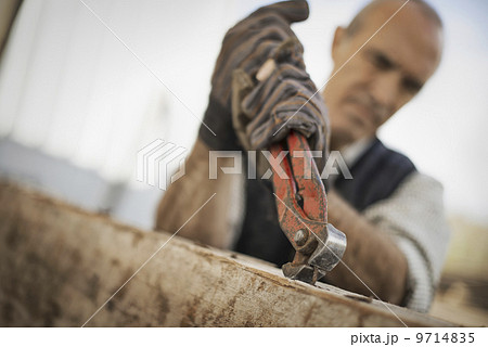 A man working in a reclaimed timber yard. Using a tool to remove metals from a reclaimed piece of timber. A man working in a reclaimed timber yard. Using a tool to remove metals from a reclaimed piece of timber. 9714835