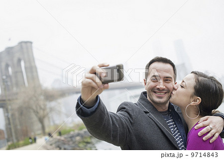 New York city. The Brooklyn Bridge crossing over the East River. A couple taking a picture with a phone, a selfy of themselves. 9714843