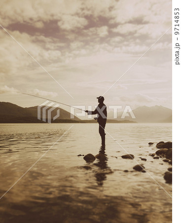 Silhouette of a man flyfishing in calm waters on the Waschusett inlet in Glacier Bay national park in Alaska. 9714853