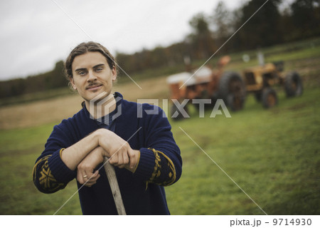 Organic Farmer at Work, A man leaning on a garden hoe. A tractor in the background. Organic Farmer at Work, A man leaning on a garden hoe. A tractor in the background. 9714930