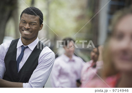 City life in spring. Young people outdoors in a city park. A man with arms folded smiling, and three other people grouped around him. 9714946