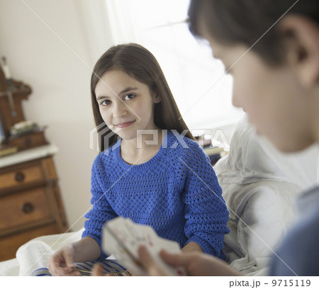 Two children at home, sitting side by side and playing a game of cards. Two children at home, sitting side by side and playing a game of cards. 9715119