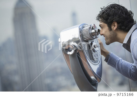 New York City. An observation deck overlooking the Empire State Building. A young man looking through a telescope over the city. 9715166